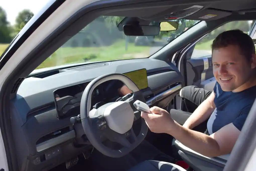 Home 8 Das Cockpit des KIA EV3 - Model 2025 - ist bei geöffneter Tür zu erkennen. Der Fahrlehrer Philip lädt ein einzusteigen und mit der Fahrstunde zu beginnen.